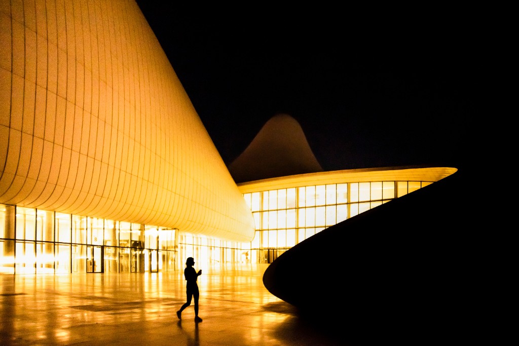 A person walking outside a warmly lit building at night